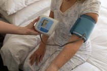 Woman at home visited by female nurse, checking blood pressure. Medical care at home during Covid 19 Coronavirus quarantine. — Stock Photo