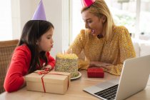 Caucasian woman and her daughter spending time at home together, celebrating birthday, using a laptop computer, making a video call. Social distancing during Covid 19 Coronavirus quarantine lockdown. — Stock Photo