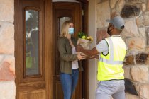 Caucasian woman spending time at home, wearing face mask, receiving a package from delivery man. Social distancing during Covid 19 Coronavirus quarantine lockdown. — Stock Photo