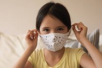 Retrato de una chica caucásica pasando tiempo en casa, usando mascarilla, mirando a la cámara. Distanciamiento social durante el bloqueo de cuarentena del Coronavirus Covid 19. - foto de stock