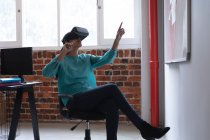 Femme de race mixte travaillant dans un bureau décontracté, portant un casque vr, un écran virtuel tactile. Distance sociale sur le lieu de travail pendant la pandémie de coronavirus Covid 19. — Photo de stock