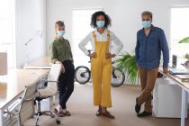 Ritratto di un gruppo multietnico di tre creativi di sesso maschile e femminile in carica che indossano maschere facciali, Salute e igiene sul posto di lavoro durante la pandemia di Coronavirus Covid 19. — Foto stock