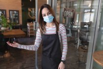 Kaukasische Friseurin, die im Friseursalon arbeitet, trägt Gesichtsmaske und begrüßt Kunden am Eingang. Gesundheit und Hygiene am Arbeitsplatz während der Coronavirus Covid 19 Pandemie. — Stockfoto