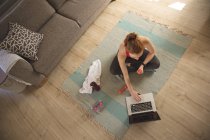 Mulher caucasiana passando tempo em casa, na sala de estar, fazendo exercícios com halteres, usando laptop. Distanciamento social durante o bloqueio de quarentena do Covid 19 Coronavirus. — Fotografia de Stock