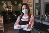 Портрет кавказької жінки-перукарки, що працює в перукарні в салоні з масками на обличчі, виставляючи фото, тримаючи перуку. Здоров 