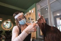 Femme coiffeuse caucasienne travaillant dans un salon de coiffure portant un masque facial, couper les cheveux d'une cliente caucasienne. Santé et hygiène sur le lieu de travail pendant la pandémie de Coronavirus Covid 19. — Photo de stock