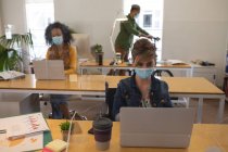 Многонациональная группа мужских и женских творческих людей, работающих на офисных столах с защитными экранами, используя ноутбуки. Здоровье и гиперактивность на рабочем месте во время коронавируса Ковид 19 пандемии. — стоковое фото
