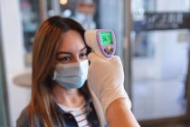 Caucasian female hairdresser working in hair salon, measuring temperature of a female Caucasian customer in face mask. Health and hygiene in workplace during Coronavirus Covid 19 pandemic. — Stock Photo