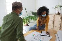 Mixed race male and female architects in office wearing face masks, discussing over architectural drawing. Health and hygiene in workplace during Coronavirus Covid 19 pandemic. — Stock Photo