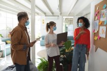 Multi ethnic group of male and female business creatives stand brainstorming in modern office wearing face masks. Health and hygiene in the workplace during Coronavirus Covid 19 pandemic. — Stock Photo