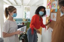 Multiethnische Gruppen von männlichen und weiblichen Kreativen stehen mit Gesichtsmasken im modernen Büro und führen Brainstorming durch. Gesundheit und Hygiene am Arbeitsplatz während der Coronavirus Covid 19 Pandemie. — Stockfoto