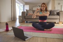 Кавказька жінка проводить час удома, у вітальні, займається фізичними вправами, практикує йогу, дивлячись на ноутбук. Соціальна дистанція в Ковиді 19 Коронавірус карантин. — стокове фото