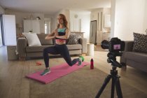 Caucasian woman spending time at home, in living room, exercising, stretching and recording it with a camera. Social distancing during Covid 19 Coronavirus quarantine lockdown. — Stock Photo