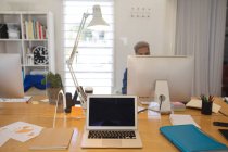 Mixte mâle créatif assis au bureau dans un bureau moderne, à l'aide d'un ordinateur, ordinateur portable au premier plan. Santé et hygiène sur le lieu de travail pendant la pandémie de Coronavirus Covid 19. — Photo de stock
