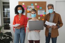Portrait of multi ethnic group of male and female creative business colleagues wearing face masks in an office. Health and hygiene in the workplace during Coronavirus Covid 19 pandemic. — Stock Photo