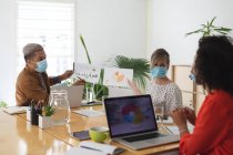 Multi ethnic group of male and female business creatives in meeting wearing face masks discussing documents. Health and hygiene in the workplace during Coronavirus Covid 19 pandemic. — Stock Photo