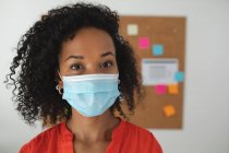 Портрет женщины-предпринимательницы смешанной расы, стоящей в офисе в маске для лица. Здоровье и гиперактивность на рабочем месте во время коронавируса Ковид 19 пандемии. — стоковое фото