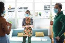 Multiethnische Gruppe männlicher und weiblicher Kreativer mit Gesichtsmasken beim Brainstorming im Büro mittels Tablet. Gesundheit und Hygiene am Arbeitsplatz während der Coronavirus Covid 19 Pandemie. — Stockfoto