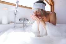 Donna caucasica trascorrere del tempo a casa, in bagno, seduto nella vasca da bagno, risciacquo maschera. Distanza sociale durante il blocco di quarantena Covid 19 Coronavirus. — Foto stock
