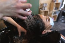 Caucasian female hairdresser working in hair salon wearing face mask, washing hair of female Caucasian customer in face mask. Health and hygiene in workplace during Coronavirus Covid 19 pandemic. — Stock Photo
