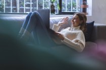 Щаслива кавказька жінка проводила вдома час, лежачи на дивані у вітальні, використовуючи ноутбук для відеодзвінків, махаючи руками. Соціальна дистанція в Ковиді 19 Коронавірус карантин. — стокове фото