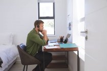 Белый мужчина проводит время дома, работает дома, пользуется ноутбуком в наушниках. Социальное дистанцирование во время изоляции коронавируса Covid 19. — стоковое фото