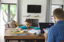 Caucasian man at home with his son together, at table in kitchen, father working using laptop computer, boy doing homework. Social distancing during Covid 19 Coronavirus quarantine lockdown. — Stock Photo
