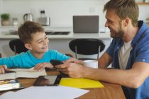 Caucasian man at home with his son together, in kitchen, father helping the boy doing homework at table. Social distancing during Covid 19 Coronavirus quarantine lockdown. — Stock Photo