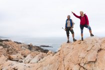 Старшая пара проводит время на природе вместе, гуляя в горах, женщина указывает вверх. активный уход на пенсию. — стоковое фото