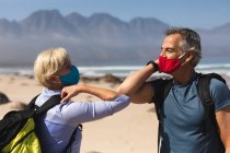 Senioren verbringen Zeit miteinander in der Natur, gehen am Strand spazieren, tragen Gesichtsmasken und grüßen sich mit Ellbogen. Gesunder Lebensstil im Ruhestand. — Stockfoto