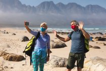 Casal sênior passando um tempo na natureza juntos, andando na praia, usando máscaras e tirando uma selfie. atividade de aposentadoria saudável. — Fotografia de Stock