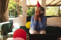 Donna caucasica anziana che passa del tempo a casa a festeggiare un compleanno, indossando un cappello da festa e usando il portatile. auto isolamento a casa durante il coronavirus covid 19 isolamento di quarantena. — Foto stock