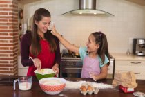 Mulher branca com sua filha assando em uma cozinha e vestindo aventais. isolamento em casa durante o bloqueio de quarentena do coronavírus covid 19. — Fotografia de Stock