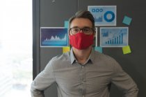 Porträt eines kaukasischen Mannes mit Gesichtsmaske, der im modernen Büro steht. Soziale Distanzierung von Quarantäne während der Coronavirus-Pandemie — Stockfoto