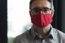 Портрет кавказца в маске для лица в современном офисе. социальная изоляция от карантина во время пандемии коронавируса — стоковое фото
