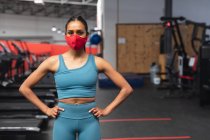 Portrait de femme caucasienne en forme portant un masque facial debout dans la salle de gym. isolement social mise en quarantaine pendant une pandémie de coronavirus — Photo de stock