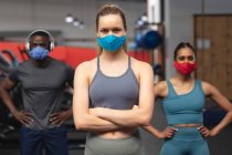 Портрет сильного африканского американца и двух белых женщин в масках, стоящих в спортзале. социальная изоляция от карантина во время пандемии коронавируса — стоковое фото