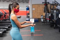 Fit caucasian woman wearing face mask sanitizing her hands in the gym. social distancing quarantine lockdown during coronavirus pandemic — Stock Photo