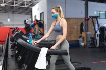 Подходящая белая женщина в маске бегущая по беговой дорожке и занимающаяся кардиотренировкой в спортзале. социальная изоляция от карантина во время пандемии коронавируса — стоковое фото