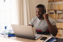 Afro-Américain utilisant un casque d'écoute téléphonique tout en ayant un chat vidéo sur ordinateur portable tout en travaillant à la maison. distanciation sociale pendant le confinement de quarantaine de coronavirus de covidé 19. — Photo de stock
