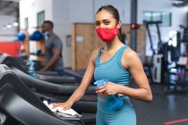 Портрет белой женщины в маске, дезинфицирующей кардио-машину перед тренировкой в спортзале. социальная изоляция от карантина во время пандемии коронавируса — стоковое фото