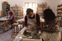 Caucasian male and mixed race female potters in face masks working in pottery studio. wearing aprons, working at a potters wheel. small creative business during covid 19 coronavirus pandemic. — Stock Photo