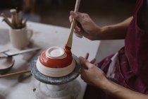Oleiro feminino trabalhando no estúdio de cerâmica. a trabalhar numa roda de oleiros, a pintar uma tigela. pequeno negócio criativo durante a pandemia do coronavírus covid 19. — Fotografia de Stock