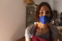 Retrato de una mujer caucásica usando mascarilla en un estudio de cerámica. pequeña empresa creativa durante la pandemia de coronavirus covid 19. - foto de stock
