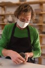 Retrato de homem caucasiano usando máscara facial no estúdio de cerâmica. pequeno negócio criativo durante a pandemia do coronavírus covid 19. — Fotografia de Stock
