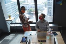 Diverse männliche und weibliche Kollegen mit Gesichtsmasken reden im modernen Büro miteinander. Soziale Distanzierung von Quarantäne während der Coronavirus-Pandemie — Stockfoto