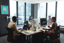 Diversos colegas con máscaras faciales en la oficina trabajando en computadoras sentadas en sus escritorios. higiene y distanciamiento social en el lugar de trabajo durante la pandemia de coronavirus covid 19. - foto de stock