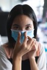 Портрет азиатской женщины в маске для лица, трогающей нос в современном офисе. социальная изоляция от карантина во время пандемии коронавируса — стоковое фото