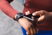 Portrait of african american woman using smartphone and smartwatch on street out and about in the city during covid 19 coronavirus pandemic. — Stock Photo
