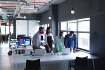 Divers collègues portant des masques faciaux à l'aide d'un ordinateur portable tout en travaillant ensemble à l'hygiène de bureau moderne et à la distance sociale sur le lieu de travail lors d'une pandémie de coronavirus 19. — Photo de stock
